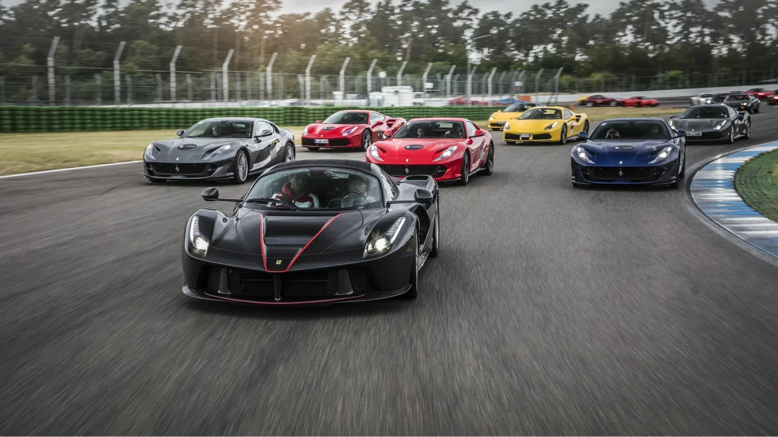 Ferrari cars driving on a circuit, led by a black LaFerrari with red accents.