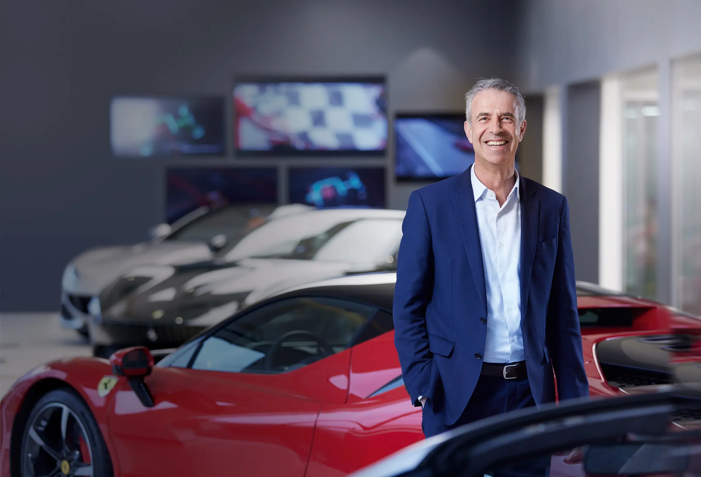 Official GOHM portrait in a showroom with sports cars in the background.