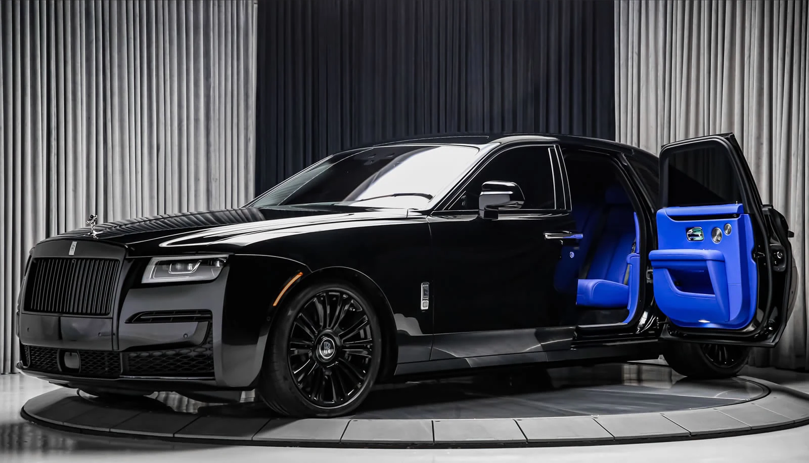 Black Rolls-Royce with blue interior and an open rear door, shown on a circular platform in the cover photograph supplied by Manhattan Motorcars in Toronto.