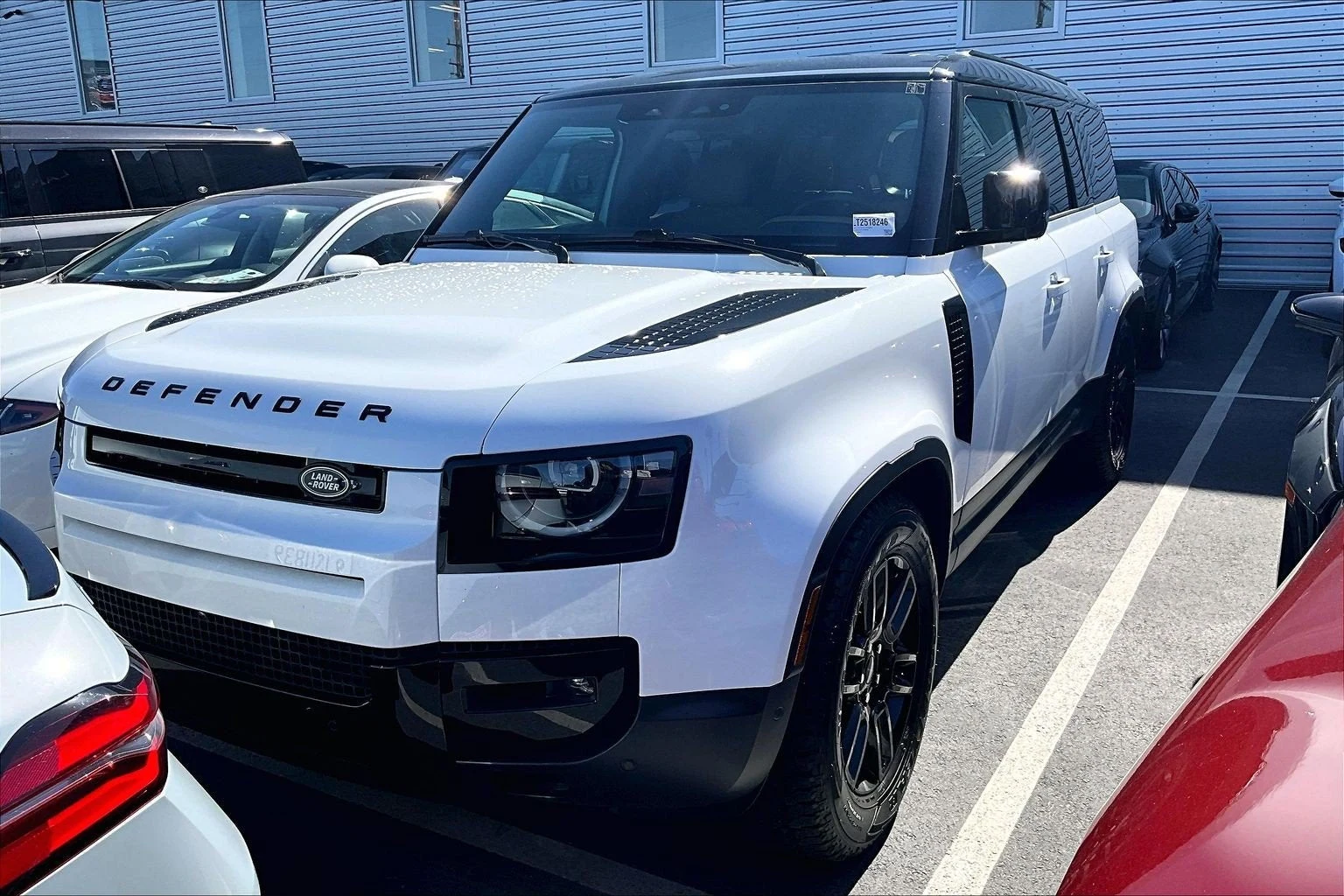 2026 Land Rover Defender 130 S, front three-quarter view with bumper corner partly obscured by a parked car